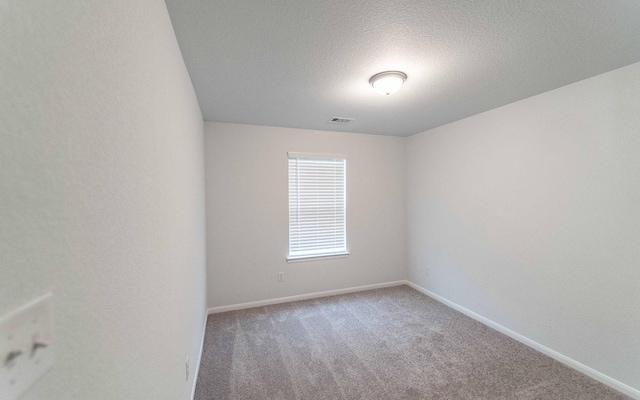 spare room with a textured ceiling, carpet, visible vents, and baseboards