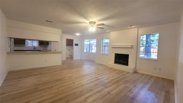 unfurnished living room with sink, a textured ceiling, ceiling fan, a fireplace, and light hardwood / wood-style floors