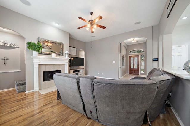 living room with a tiled fireplace, ceiling fan, and light hardwood / wood-style flooring