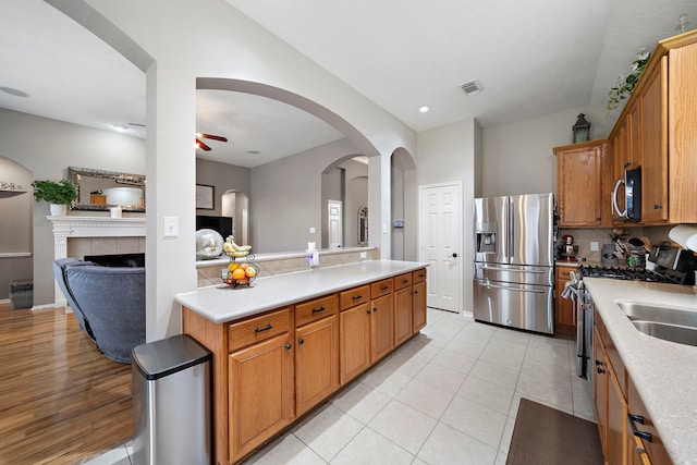 kitchen with light tile patterned flooring, tasteful backsplash, ceiling fan, stainless steel appliances, and a tiled fireplace