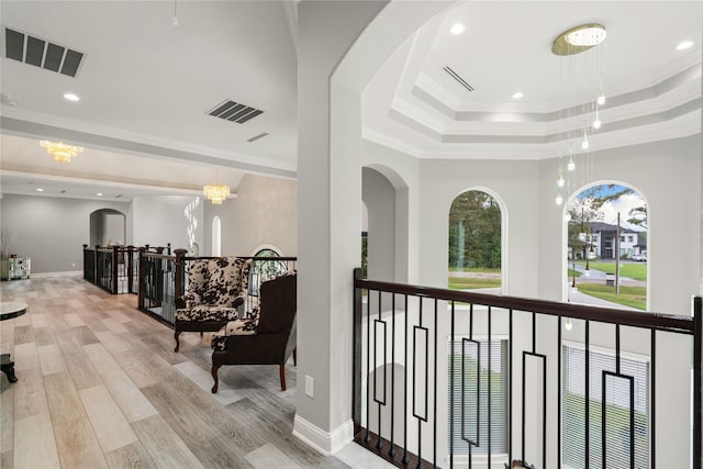 corridor featuring a raised ceiling, ornamental molding, and light wood-type flooring