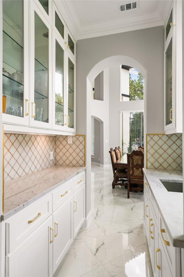 kitchen featuring light stone counters, white cabinetry, tasteful backsplash, and crown molding