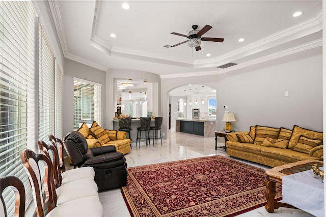 living room featuring ceiling fan, ornamental molding, and a raised ceiling