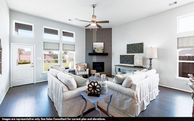 living room featuring ceiling fan, a large fireplace, and dark hardwood / wood-style flooring