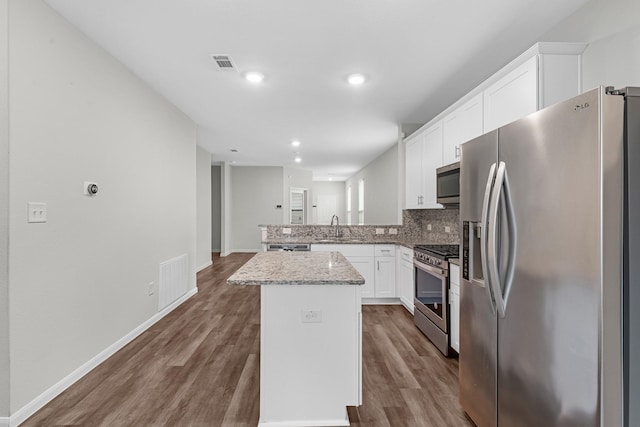 kitchen with appliances with stainless steel finishes, white cabinetry, backsplash, a center island, and light stone counters