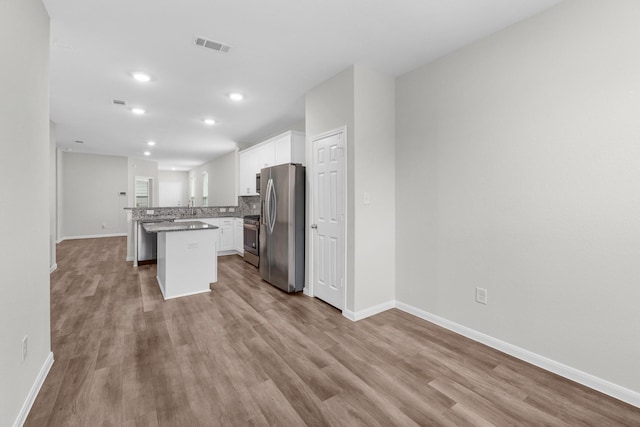 kitchen with a center island, light wood-type flooring, kitchen peninsula, stainless steel appliances, and white cabinets