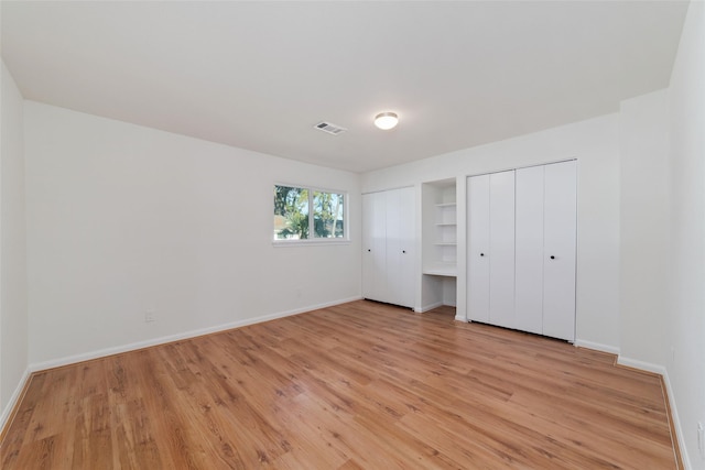 unfurnished bedroom with multiple closets and light hardwood / wood-style flooring