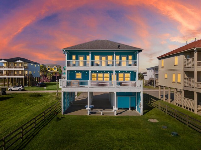 back house at dusk featuring a patio, a balcony, and a lawn