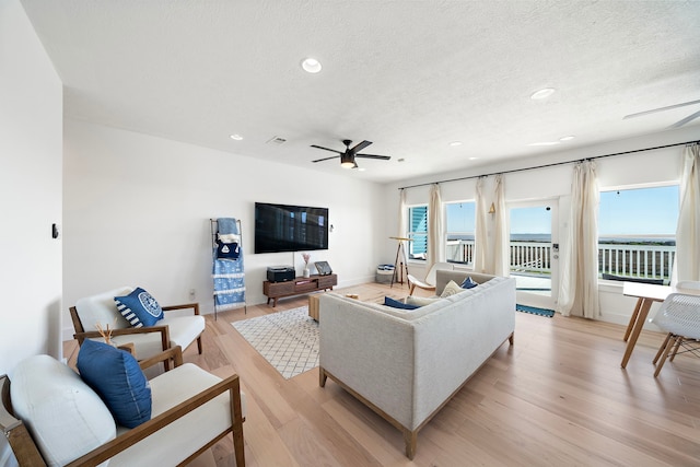 living room featuring light hardwood / wood-style flooring, a textured ceiling, plenty of natural light, and ceiling fan