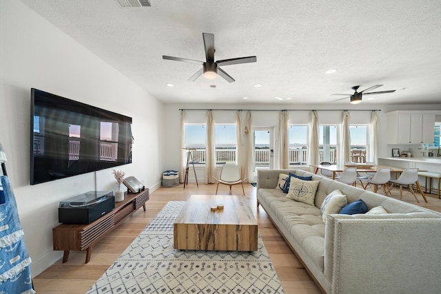 living room featuring a textured ceiling, light hardwood / wood-style floors, and ceiling fan