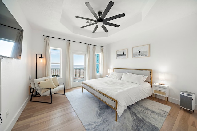 bedroom with ceiling fan, access to exterior, a raised ceiling, and light hardwood / wood-style flooring