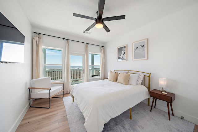 bedroom featuring ceiling fan, a water view, access to exterior, and light wood-type flooring