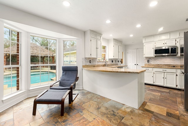 kitchen with sink, white cabinetry, light stone counters, kitchen peninsula, and decorative backsplash