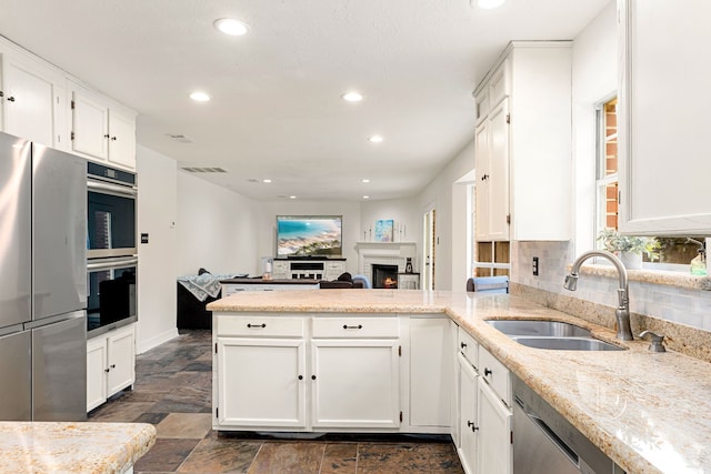 kitchen with sink, white cabinetry, stainless steel appliances, light stone counters, and kitchen peninsula