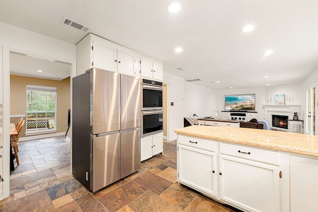 kitchen with white cabinetry, light stone counters, a fireplace, and stainless steel appliances