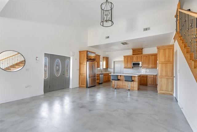 kitchen with hanging light fixtures, a towering ceiling, a kitchen breakfast bar, stainless steel appliances, and a center island