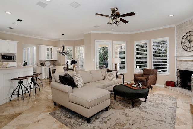 living room with a brick fireplace, crown molding, and ceiling fan with notable chandelier