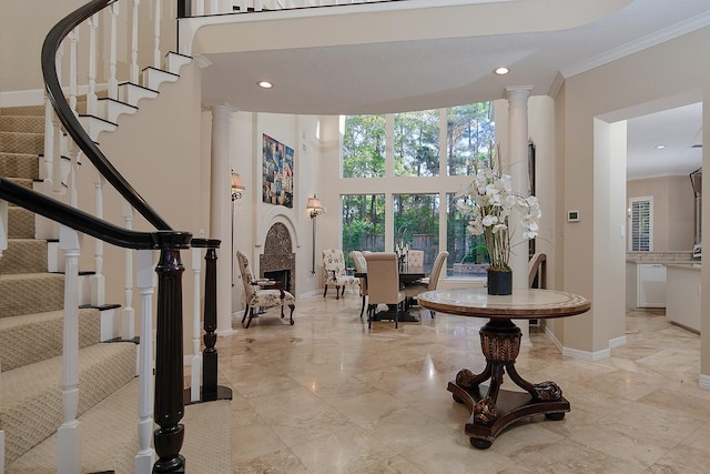 entryway featuring a towering ceiling, ornamental molding, and decorative columns