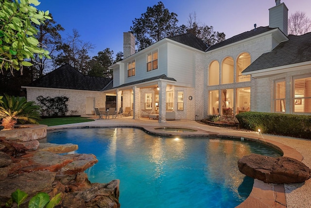 pool at dusk featuring an in ground hot tub and a patio area