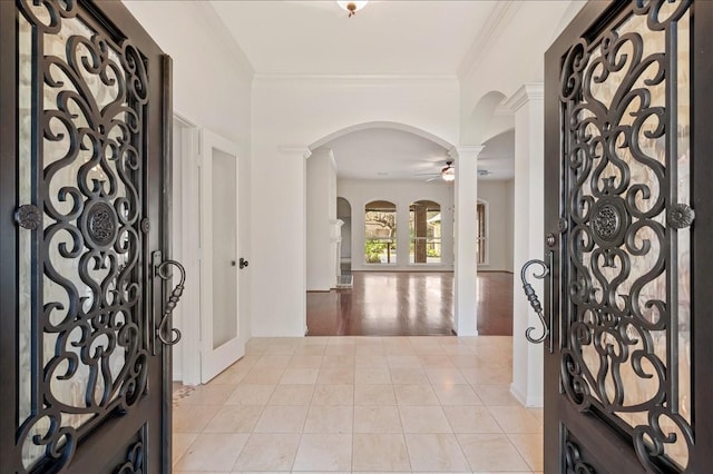 tiled foyer featuring ceiling fan, ornamental molding, and decorative columns