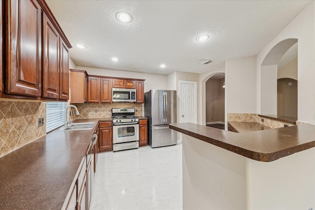 kitchen with sink, tasteful backsplash, a textured ceiling, appliances with stainless steel finishes, and kitchen peninsula