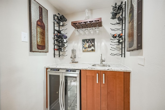 bar with beverage cooler, light stone countertops, and sink