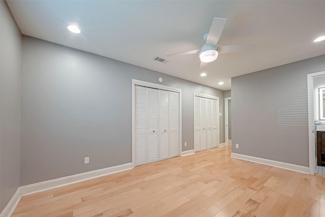 unfurnished bedroom featuring two closets, light hardwood / wood-style floors, and ceiling fan