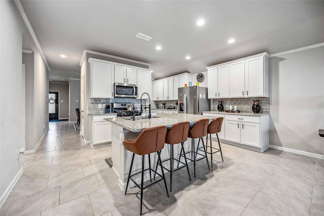 kitchen with sink, appliances with stainless steel finishes, white cabinetry, light stone counters, and a center island with sink