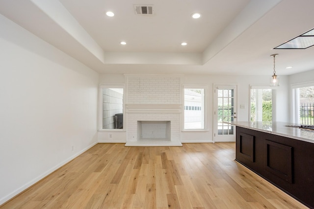 unfurnished living room featuring a brick fireplace, a raised ceiling, and light wood-type flooring