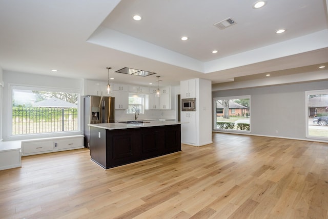 kitchen with white cabinetry, a center island, a tray ceiling, pendant lighting, and stainless steel appliances