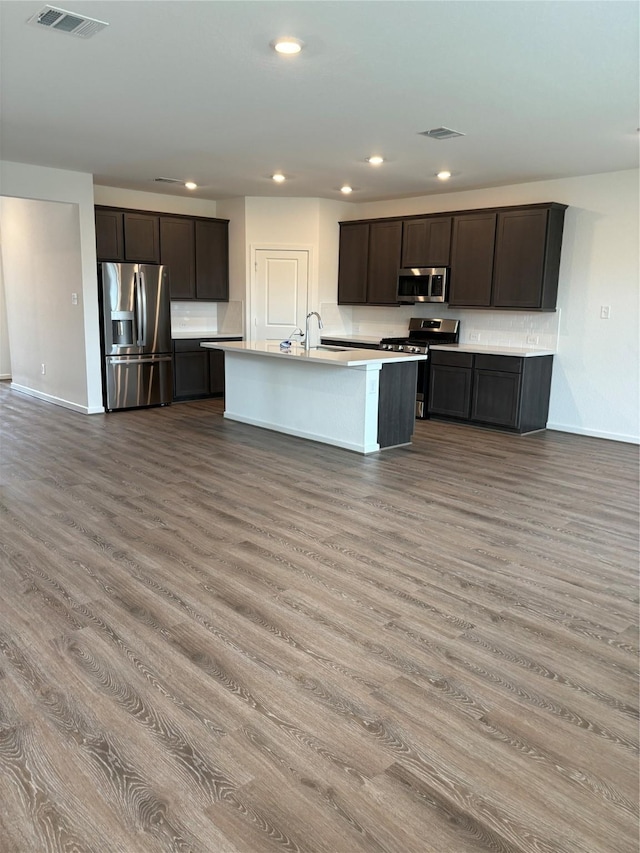 kitchen with stainless steel appliances, a kitchen island with sink, dark brown cabinets, and light hardwood / wood-style flooring