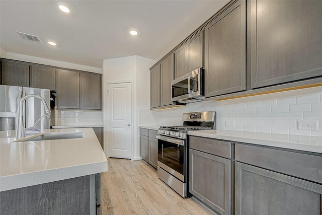 kitchen with visible vents, stainless steel appliances, light countertops, light wood-type flooring, and a sink