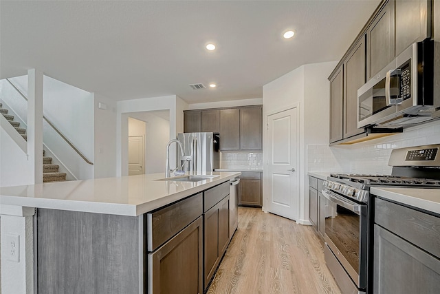 kitchen featuring light wood-type flooring, a kitchen island with sink, appliances with stainless steel finishes, and light countertops