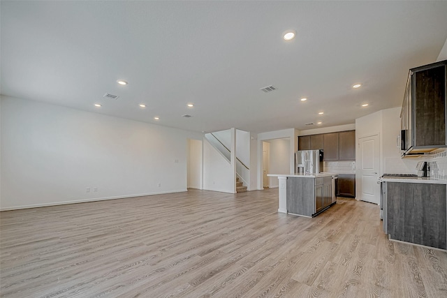 kitchen with a kitchen island with sink, open floor plan, light countertops, and stainless steel fridge with ice dispenser