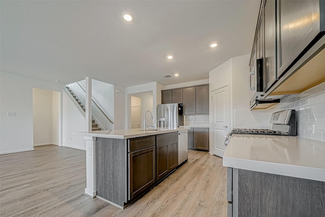 kitchen with an island with sink, light wood finished floors, stainless steel appliances, and light countertops