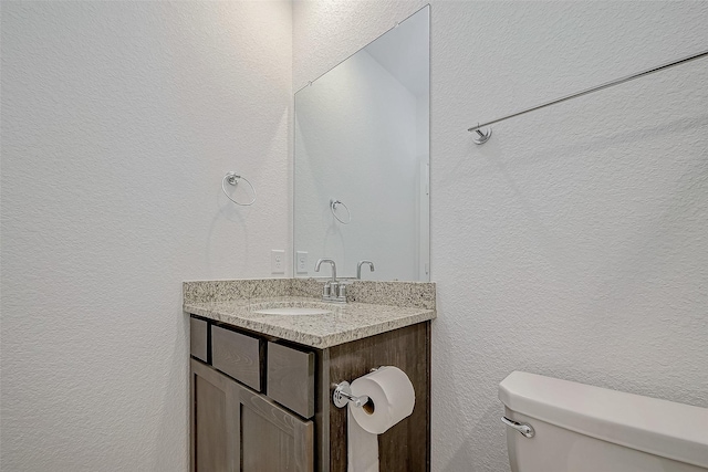 bathroom with a textured wall, vanity, and toilet