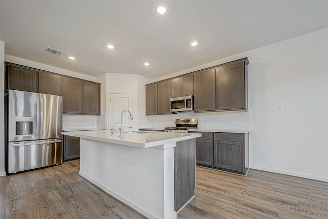 kitchen featuring stainless steel appliances, light countertops, visible vents, a sink, and an island with sink