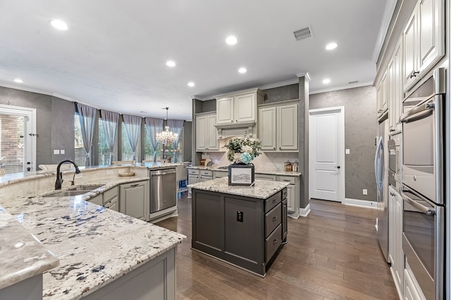 kitchen featuring visible vents, appliances with stainless steel finishes, light stone counters, a center island, and a sink