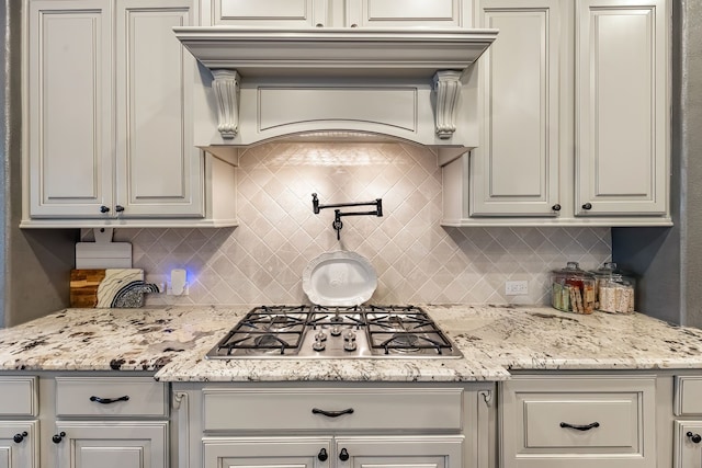 kitchen featuring light stone counters, stainless steel gas stovetop, backsplash, and custom exhaust hood