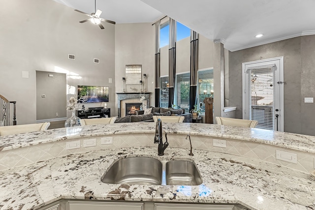 kitchen featuring a sink, visible vents, open floor plan, light stone countertops, and a glass covered fireplace