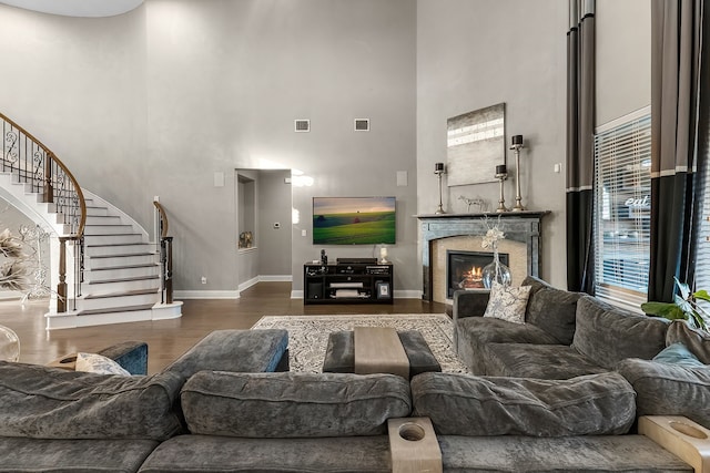 living area featuring dark wood-style floors, visible vents, stairway, a glass covered fireplace, and baseboards