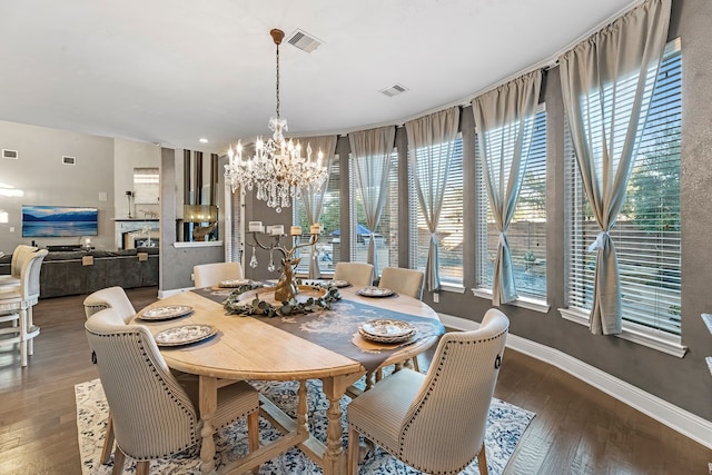 dining space with a glass covered fireplace, dark wood finished floors, visible vents, and a notable chandelier