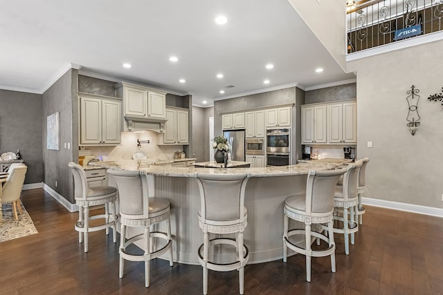 kitchen with light stone countertops, stainless steel appliances, cream cabinetry, and a kitchen breakfast bar