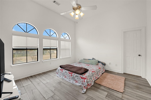 bedroom with hardwood / wood-style flooring, a high ceiling, and ceiling fan