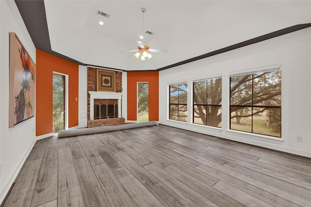 unfurnished living room featuring a raised ceiling, a brick fireplace, ceiling fan, and light hardwood / wood-style flooring