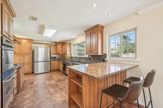 kitchen with a breakfast bar area, stainless steel appliances, light stone countertops, decorative backsplash, and kitchen peninsula