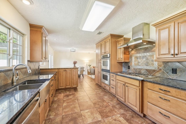 kitchen with sink, tasteful backsplash, appliances with stainless steel finishes, dark stone counters, and wall chimney range hood