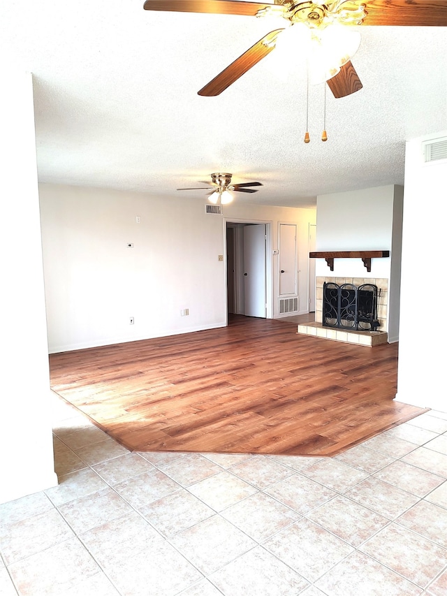 unfurnished living room featuring ceiling fan, light tile patterned floors, a textured ceiling, and a fireplace