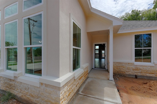 doorway to property with stone siding, stucco siding, and roof with shingles