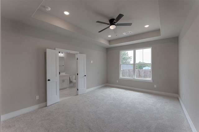 unfurnished bedroom featuring baseboards, visible vents, a tray ceiling, recessed lighting, and light carpet